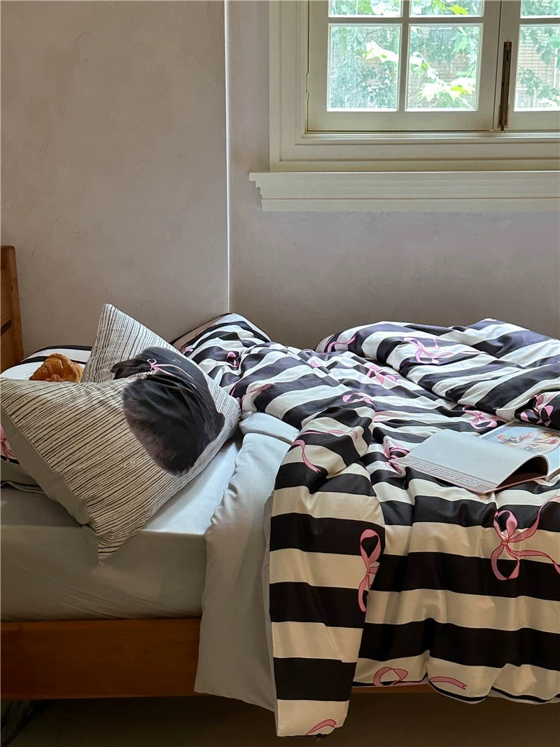 Bed with black and white striped bedding and pink accents, near a window.