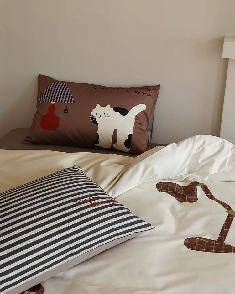 Bed with striped pillow and brown pillow featuring a cat design.