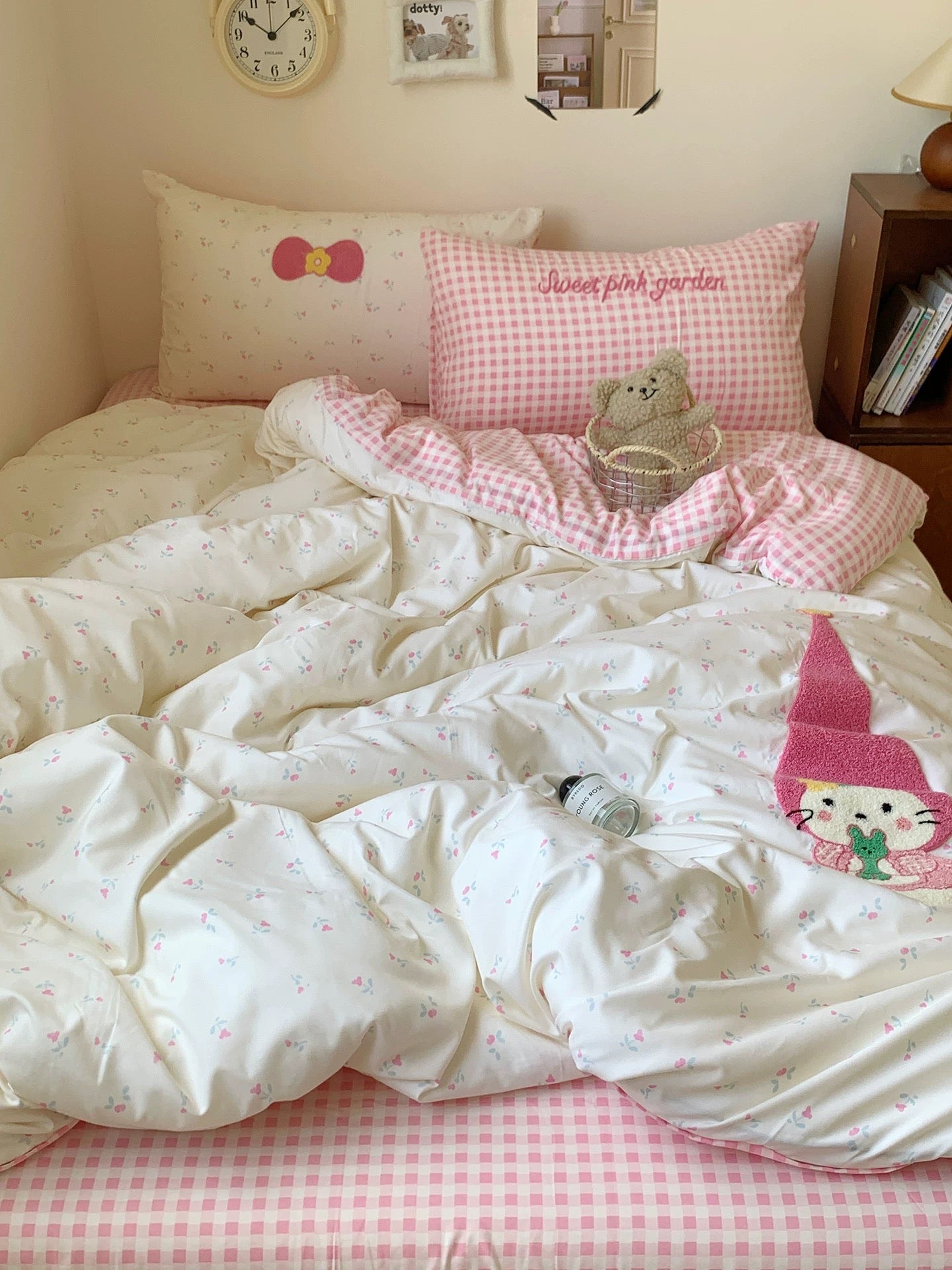 Bed with white comforter, pink checkered sheets, and decorative pillows in a bedroom setting.