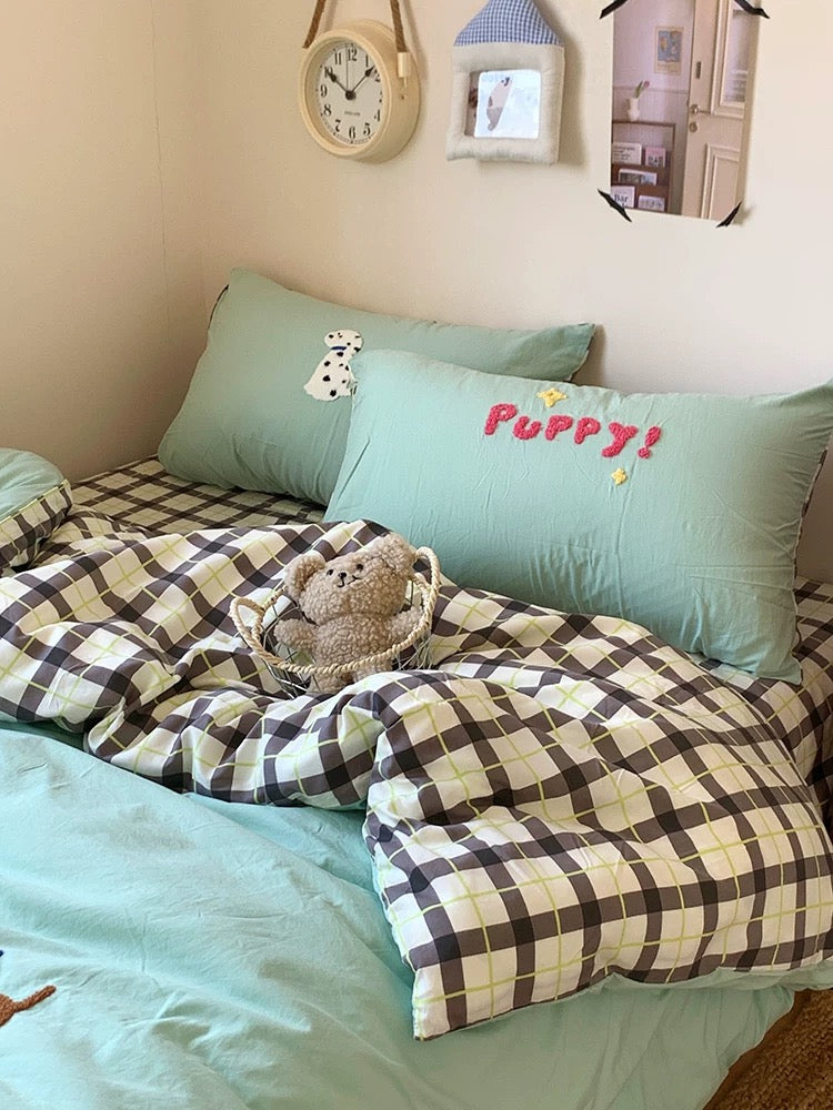 Bed with checkered blanket, teddy bear, and pillows with 'Puppy!' text.