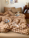 Brown plaid comforter on a bed with pillows and books in the background