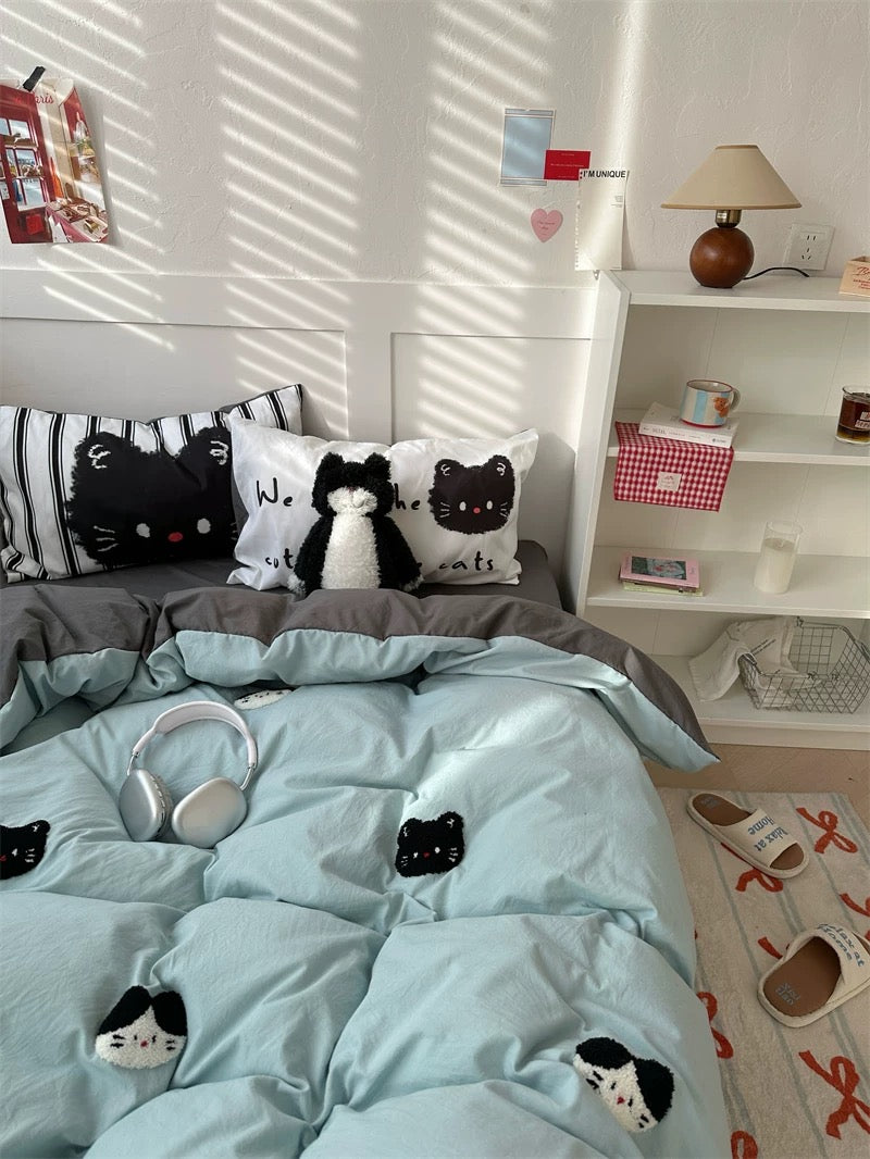 Bedroom with light blue bedding featuring cat designs, a shelf with decorative items, and a rug on the floor.