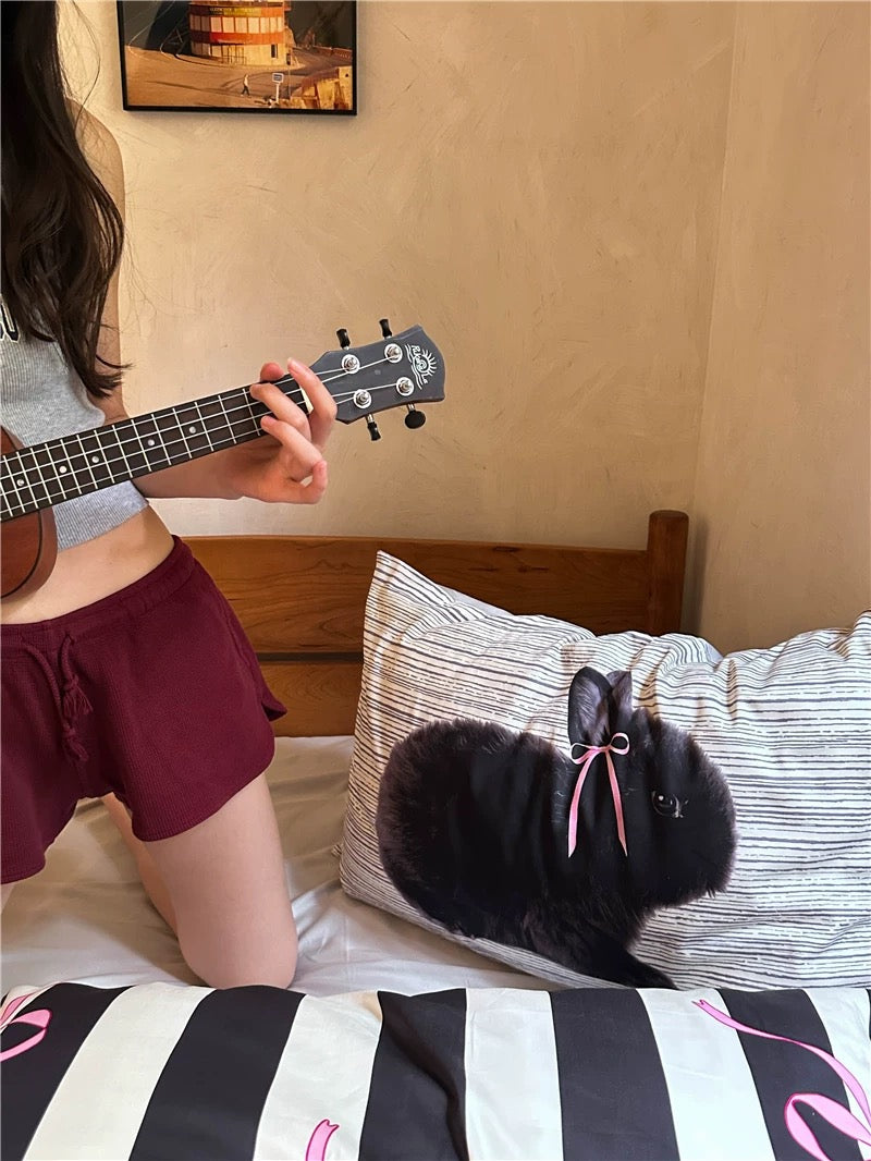 Person playing a ukulele on a bed with a black rabbit wearing a pink bow.