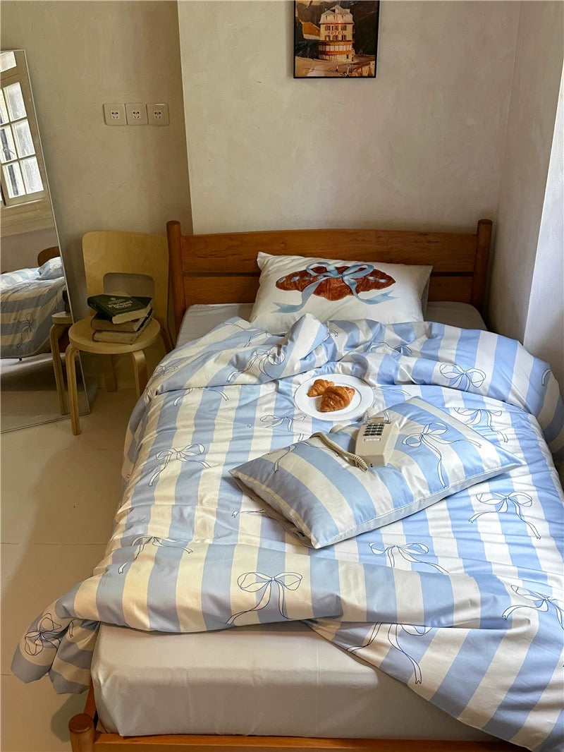 Bed with striped bedding and a pillow in a room with a window and wall art.