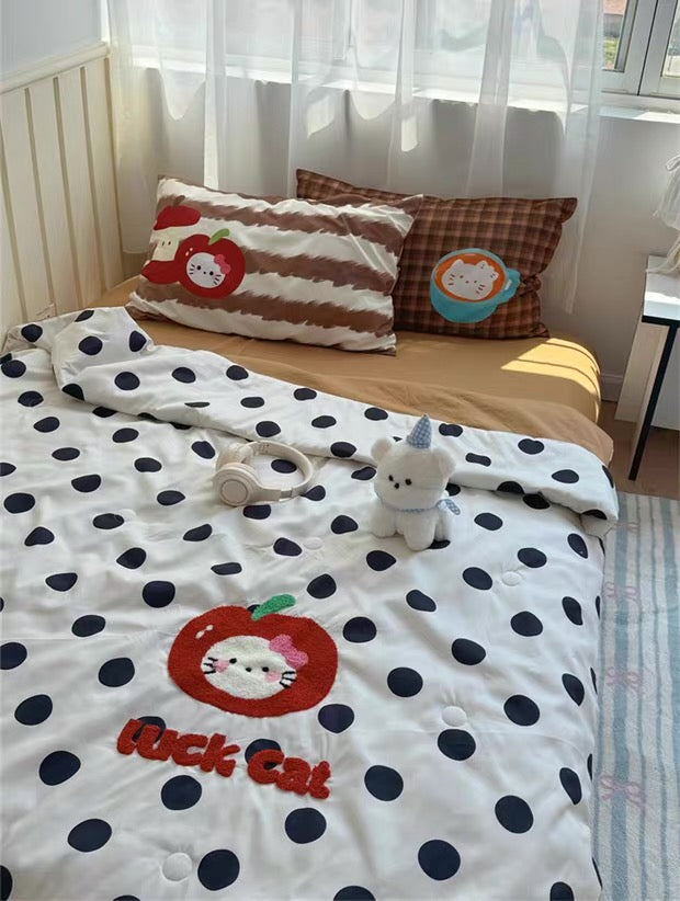 Children's bedroom with polka dot blanket, cat-themed pillows, and stuffed toy.