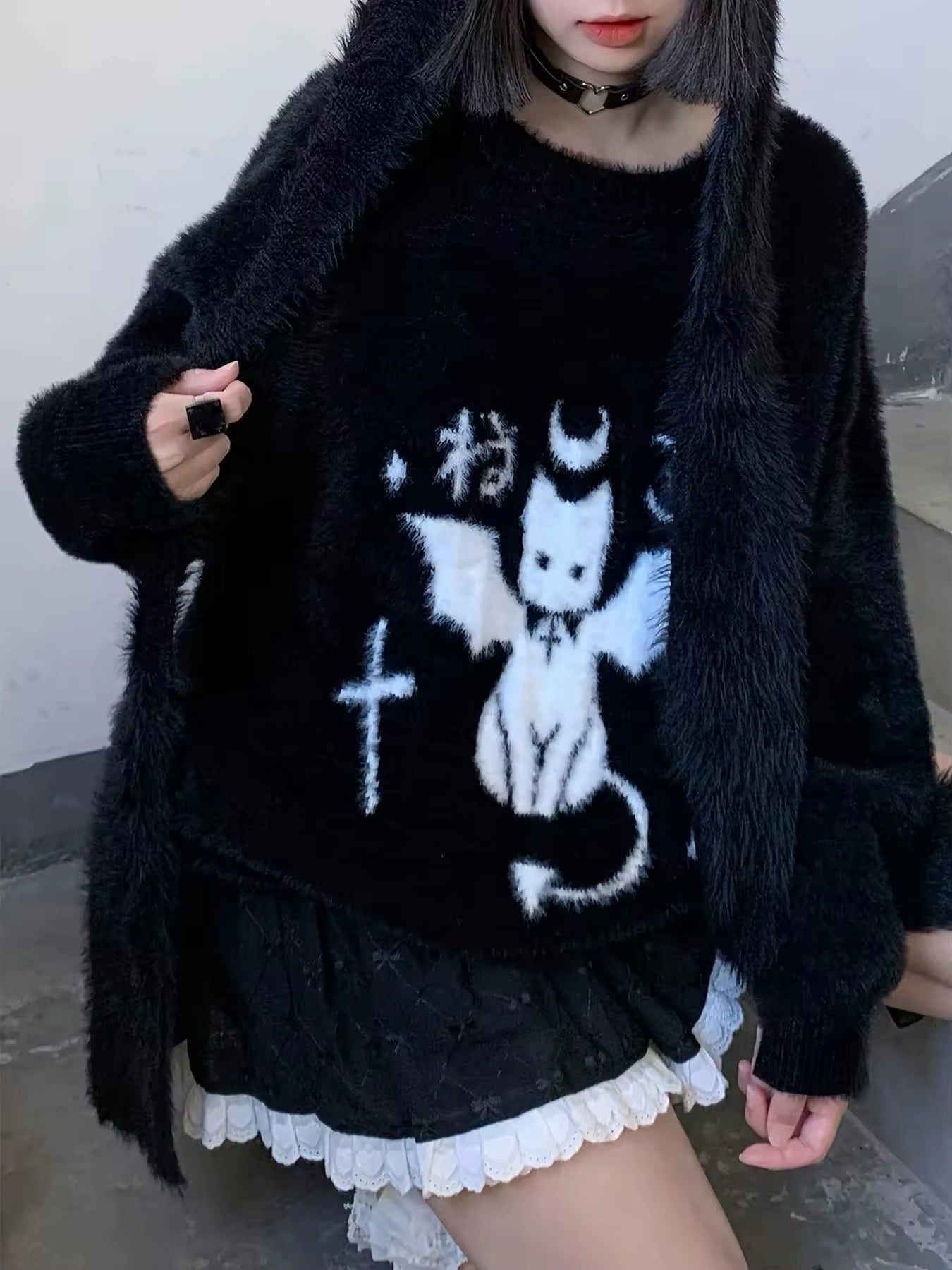 Model wearing a black oversized knit sweater with white devil cat graphic and spooky aesthetic room decor