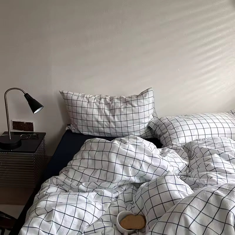 Bed with grid-patterned bedding and pillows in a room with a lamp and nightstand.