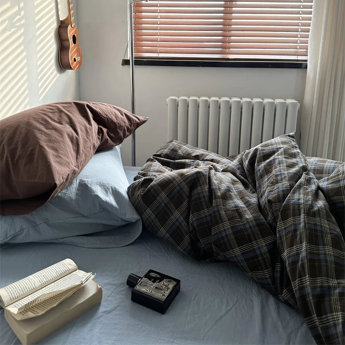 Bedroom with plaid blanket, book, and bottle on a bed with pillows.