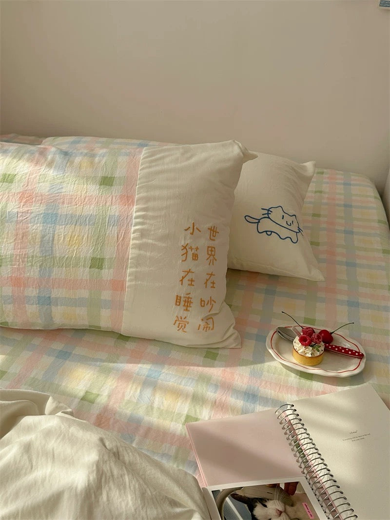 Bed with checkered bedding, decorative pillows, and a small plate with a dessert.