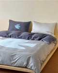 Gray bedding set with a blue bird design on a bed against a beige wall.