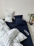 Navy bedspread with striped pillows and a plant on a nightstand.
