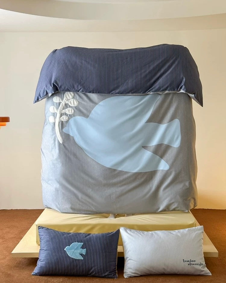 Bed with gray comforter featuring a whale design, blue and white pillows on a wooden floor.