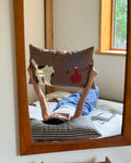 Person lying on a bed with cartoon pillow, reflected in a mirror.