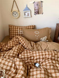 Brown plaid bedding set on a bed with pillows and a teddy bear, in a room setting.