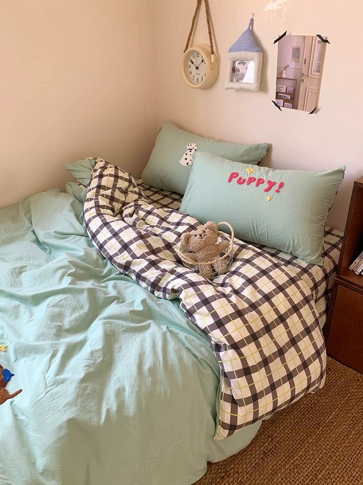 Bedroom with a bed covered in green bedding and plaid blanket, featuring a pillow with 'Puppy!' text.