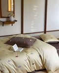 Beige bedspread with colorful patterns on a bed in a room with a wooden shelf and mirror.
