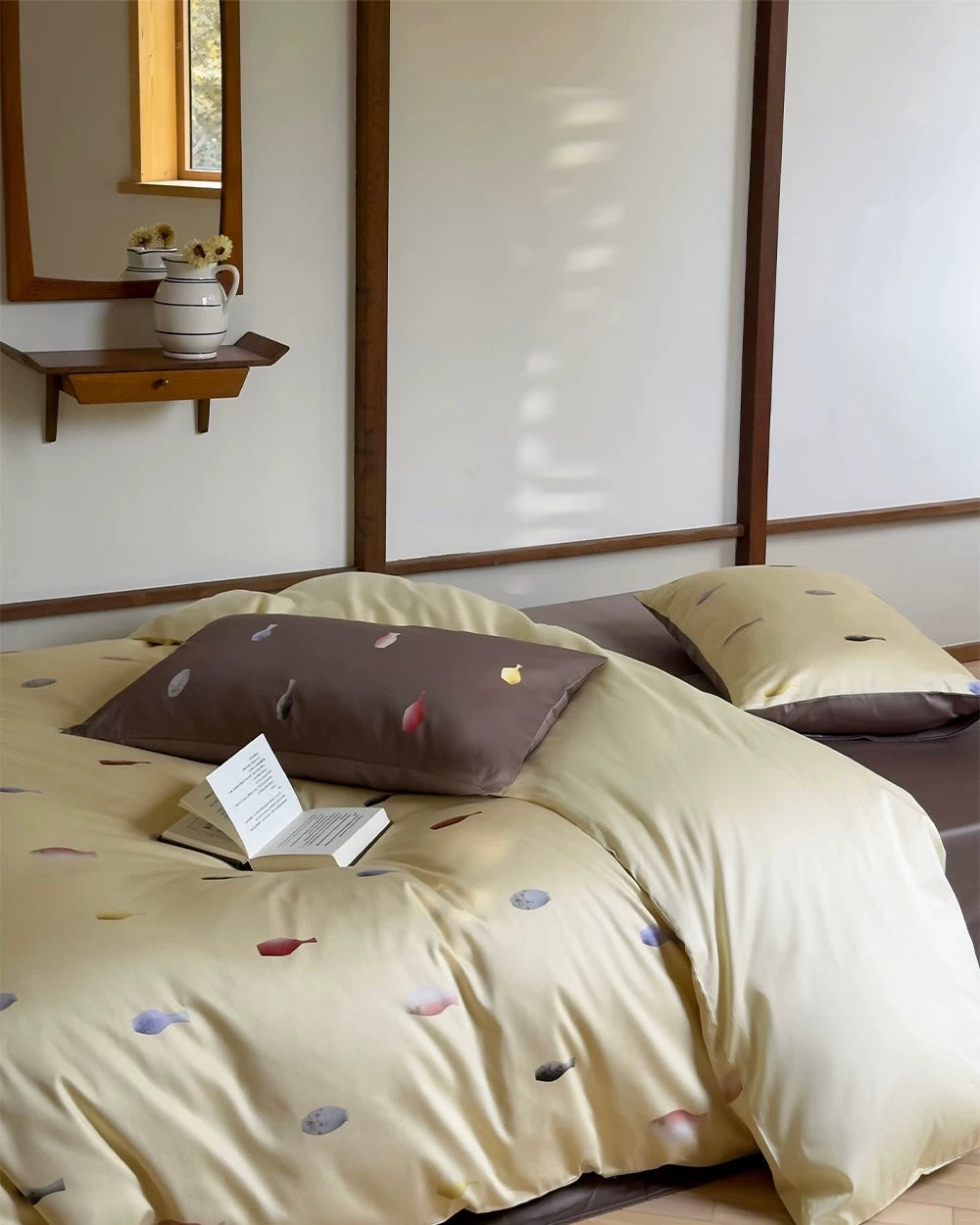 Beige bedspread with colorful patterns on a bed in a room with a wooden shelf and mirror.