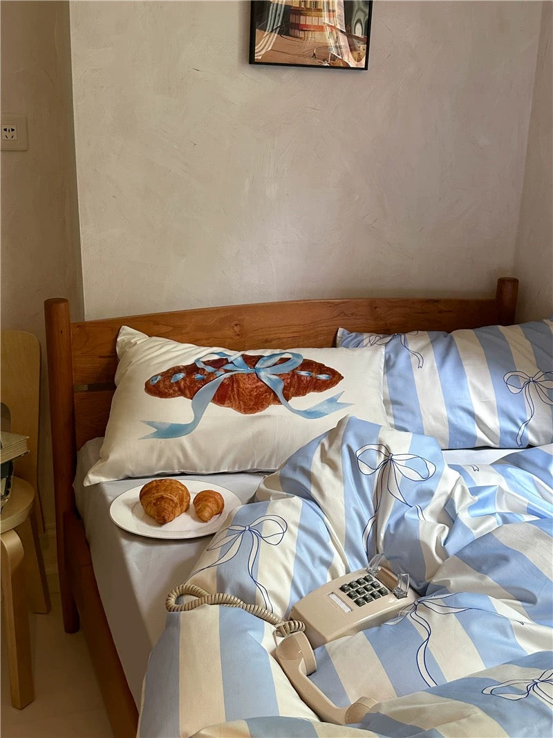 Bed with blue and white striped bedding, a plate of pastries, and a telephone on a nightstand.