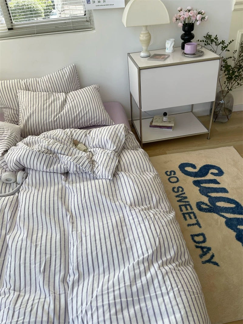 Bedroom with striped bedding, nightstand, and decorative rug.