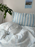 Floral-patterned bedding with a striped pillow on a bed, plant and poster in the background.