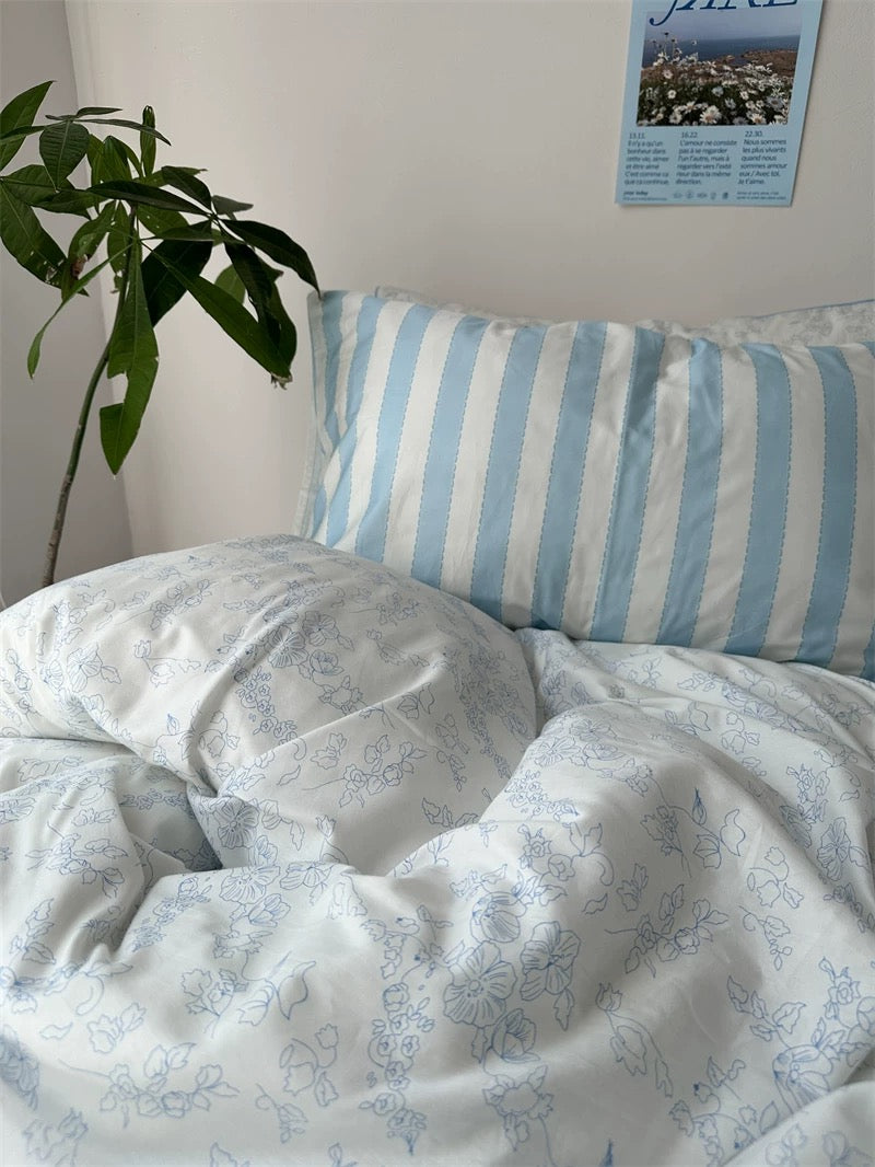 Floral-patterned bedding with a striped pillow on a bed, plant and poster in the background.
