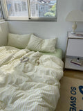 Bedroom with a bed covered in white bedding, a nightstand with a lamp, and a window with blinds.