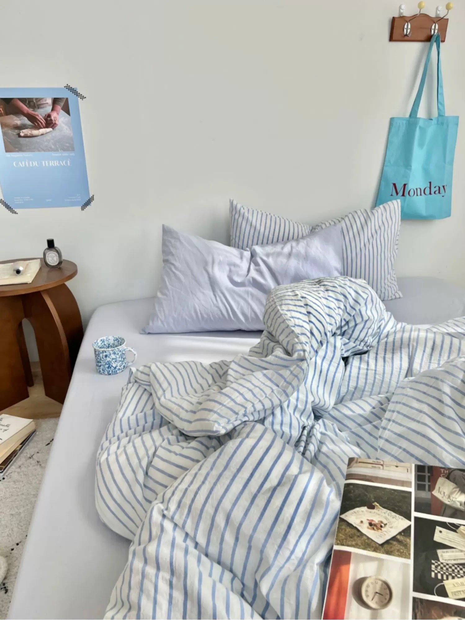 Bed with striped bedding in a room with a calendar, bag, and books on a table.