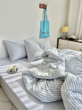 Bed with striped bedding and pillows, light blue bag hanging on wall, and small table with items.