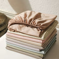 Stack of folded pastel-colored bed sheets on a white surface.