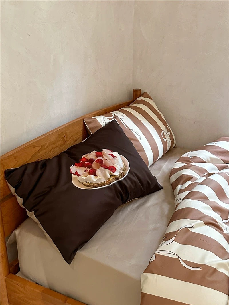 Bed with brown and white striped bedding and pillows, featuring a dessert on one pillow.