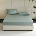 Bed with light green bedding and pillows in a minimalistic room.