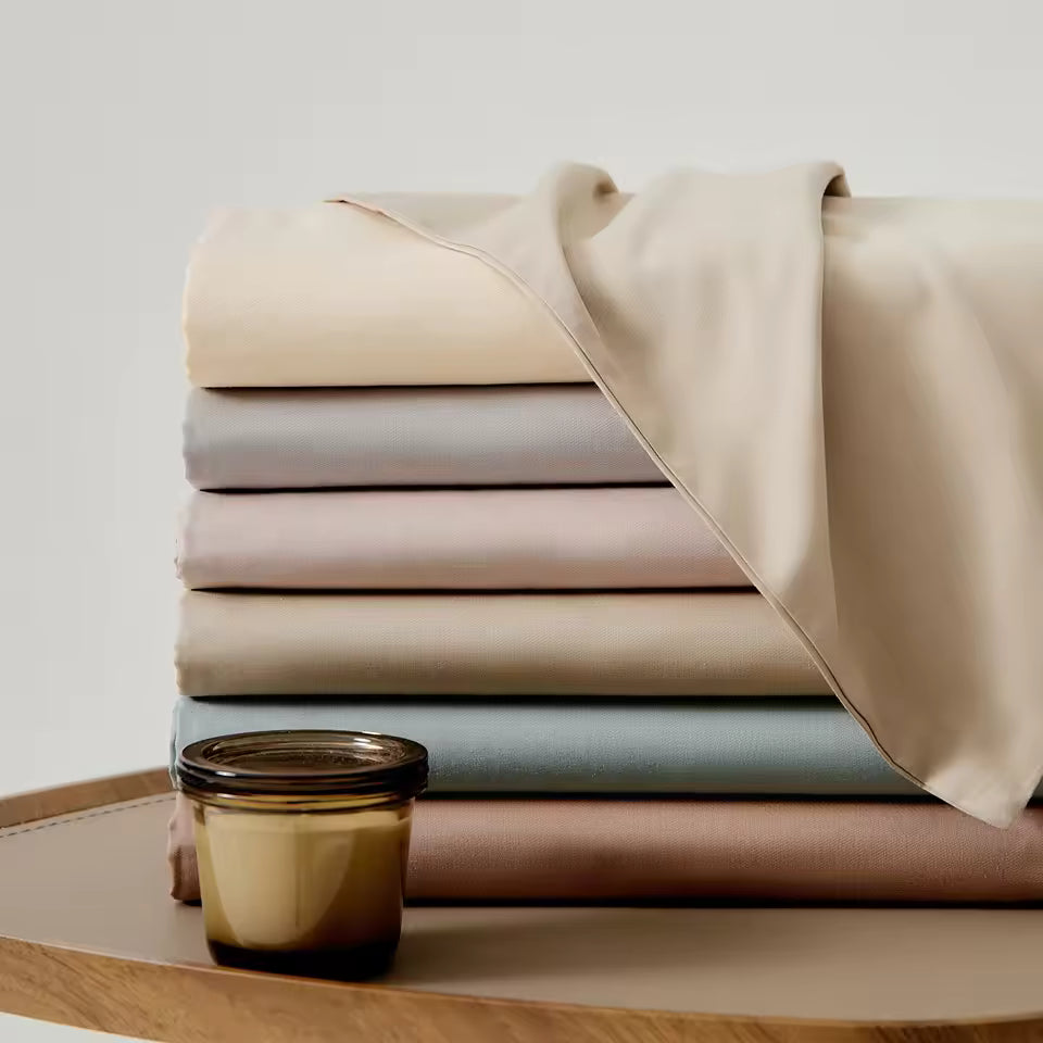Stack of folded beige, gray, and brown fabrics on a wooden surface with a small jar.