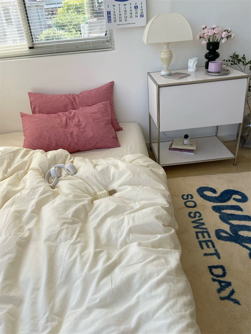 Bedroom with white bedding, red pillows, and a nightstand with a lamp.