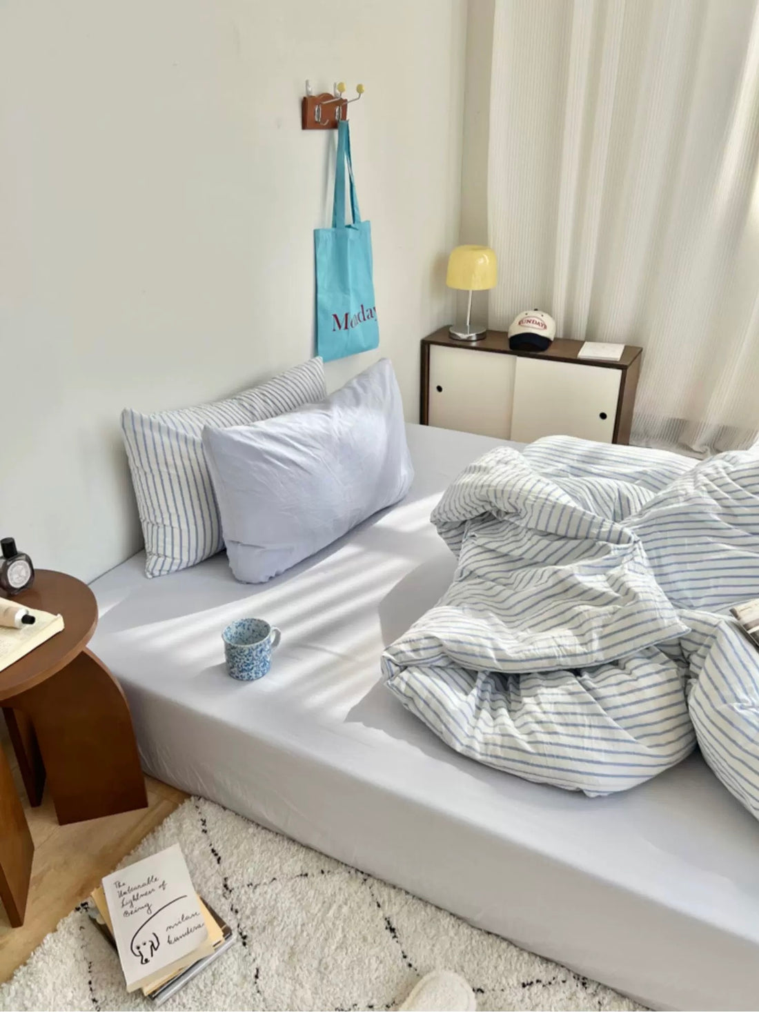 Bedroom with a bed covered in striped bedding, pillows, and a nightstand with a lamp.