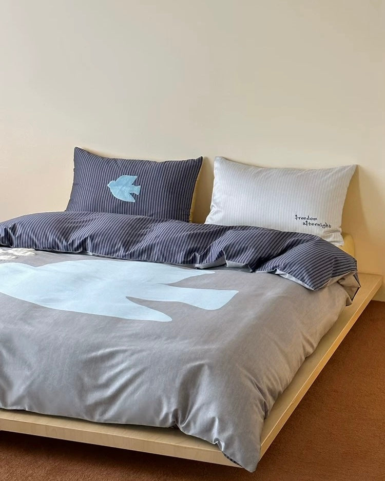 Bed with gray bedding and pillows against a beige wall