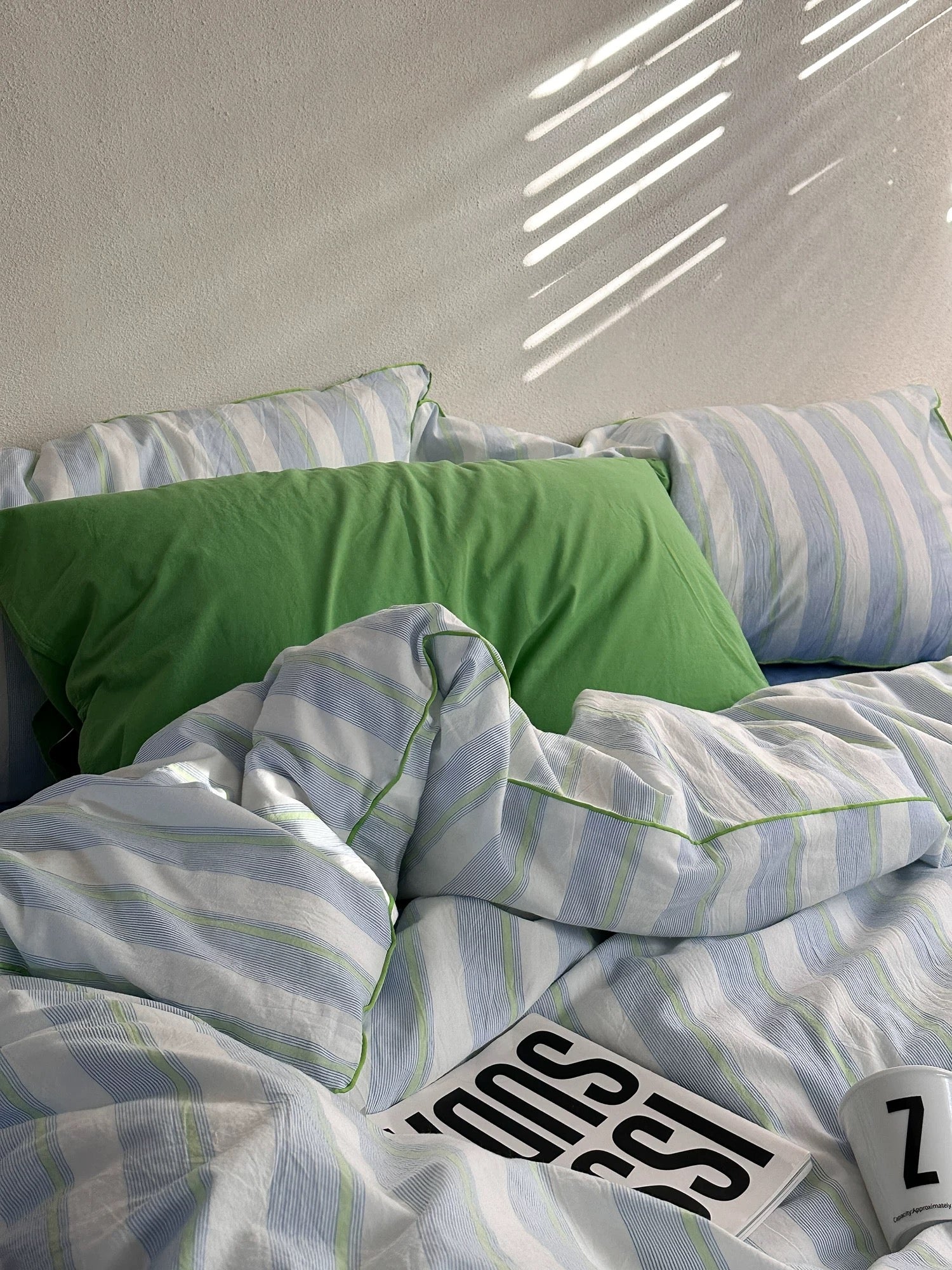 Striped bedding with a green pillow on a bed, featuring the brand 'Snoozies'.