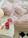 Striped bedding with a visible brand name on a bed, next to a plastic bag and jar on a surface.
