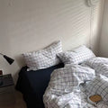 Bed with checkered bedding and pillows in a room with a lamp and wall.
