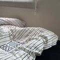 Striped bedding on a bed with a plain wall and window blinds in the background