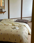 Beige bedspread with colorful leaf pattern on a bed in a bedroom setting.