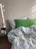 Bed with striped bedding and green pillow, nightstand with lamp in the corner