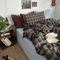 Plaid blanket and pillows on a bed in a cozy room with a side table and books.