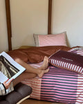 Person sitting on a bed holding a book, with striped bedding and a wooden headboard.