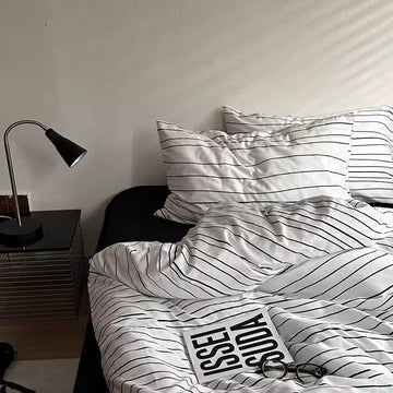 Bed with striped bedding and a lamp on a nightstand in a bedroom.