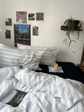 Bedroom with striped bedding, photos on the wall, and a plant.