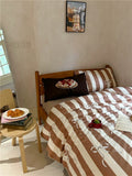 Bedroom with a bed covered in brown and beige striped bedding, pillows, and small table with food.