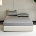 Gray mattress cover with pillows on a bed in a minimalistic room.