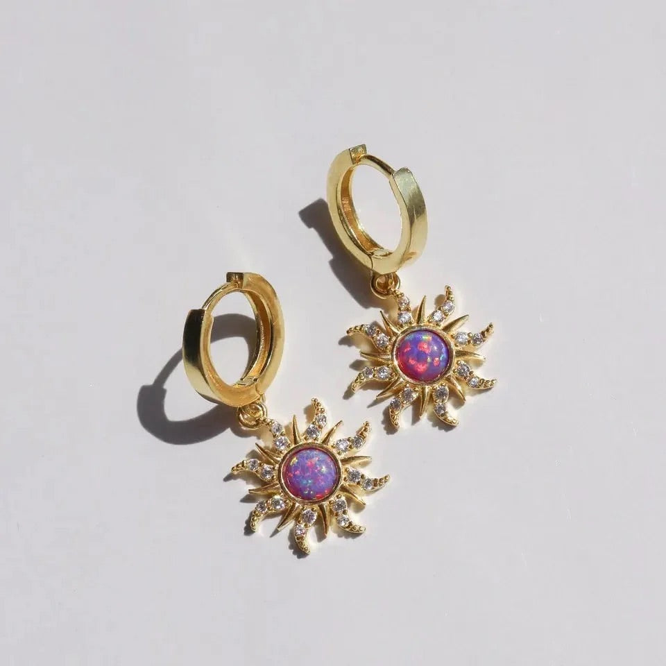 Gold jewelry set with opal sun charms, including necklace, ring, and earrings on pink velvet background.