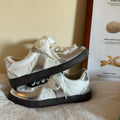White sneakers with black soles on a surface with a paper in the background