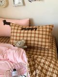 Bed with brown and pink checkered bedding, teddy bear, and decorative pillows.